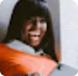 Smiling person with long straight hair wearing an orange garment.